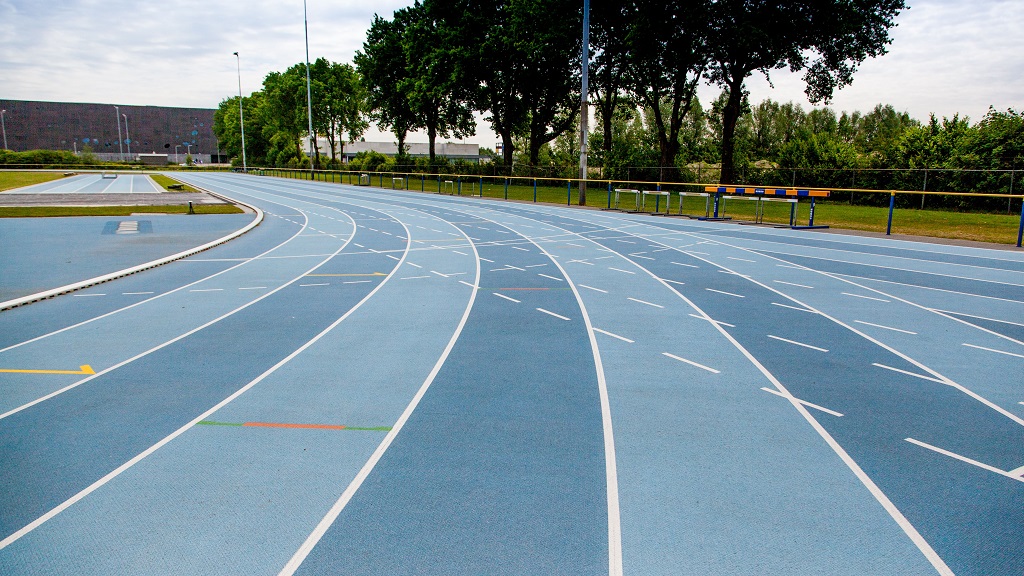 blauwe atletiekbaan met op de achtergrond T-Kwadraat